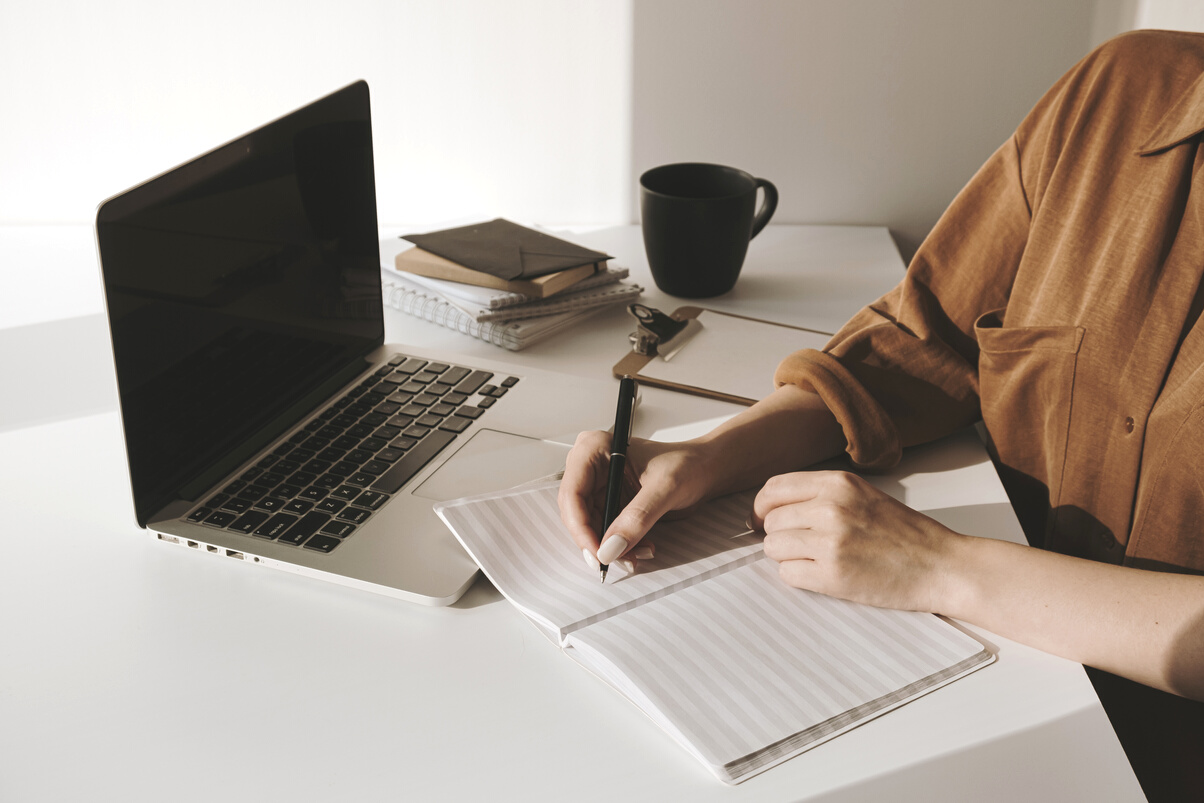 Woman Writing on Notebook on the Table with Laptop